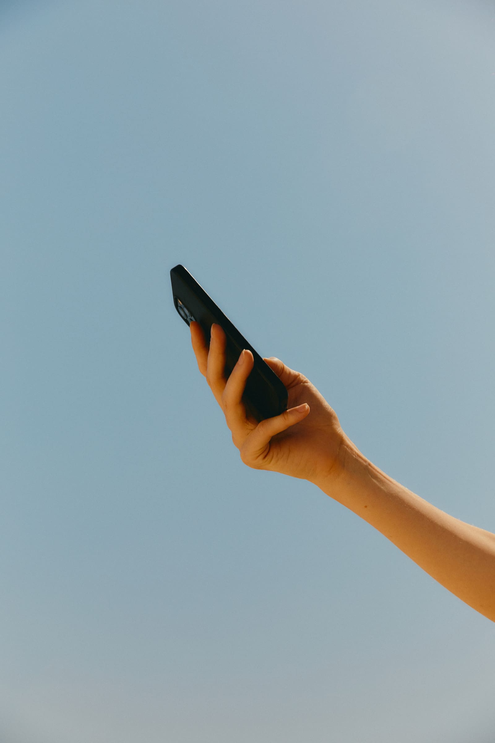 Hand holding a phone against a blue sky, checking an Instagram profile