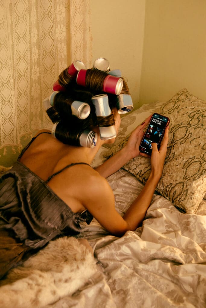 Woman in hair rollers typing a note on her phone in bed, capturing content ideas before they disappear