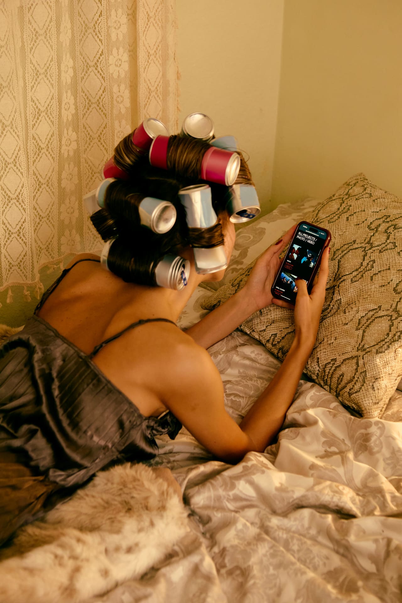 Woman in hair rollers typing a note on her phone in bed, capturing content ideas before they disappear