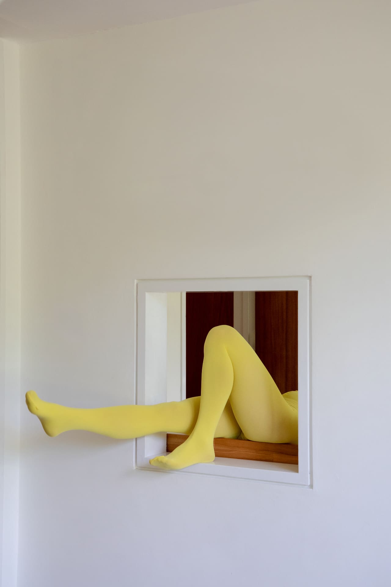 Legs in yellow tights through a wall hatch, like a visitor landing in the wrong place on an Instagram profile